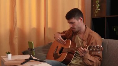 Evde gitar çalan genç bir müzisyen. Yetişkin gitarist odada oturmuş akustik gitar çalıyor, sosyal medya için akıllı telefondan video kaydediyor..