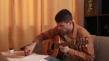 Evde gitar çalan genç bir müzisyen. Yetişkin bir gitarist odada oturup akustik gitar çalıyor, beste yapıyor ve nota kağıdına yazıyor. Hobi ve boş zaman kavramı.