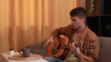 Evde gitar çalan genç bir müzisyen. Yetişkin bir gitarist odada oturup akustik gitar çalar, melodi besteler, akorlar çalar, çay içer. Hobi ve boş zaman kavramı.