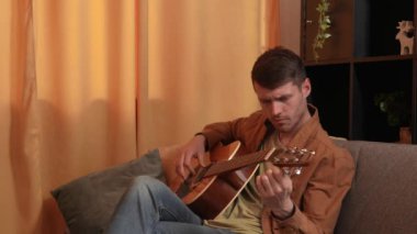 Evde gitar çalan genç bir müzisyen. Yetişkin gitarist odada oturup akustik gitar çalıyor, telleri sıkıyor ve enstrümanı kuruyor. Hobi ve boş zaman kavramı.