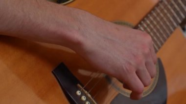 Evde gitar çalan genç bir müzisyen. Yetişkin bir gitarist akustik gitar çalıyor, erkek eli ve gitar tıngırdatan parmakları yakından çekiyor. Hobi ve boş zaman kavramı.