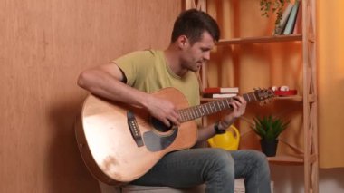 Evde gitar çalan genç bir müzisyen. Yetişkin bir gitarist odada oturup akustik gitar çalıyor, şarkı söylüyor, akorları parmaklıyor. Sürecin tadını çıkarır Yavaş çekim.