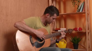 Evde gitar çalan genç bir müzisyen. Yetişkin bir gitarist odada oturup akustik gitar çalıyor enerjik şarkılar çalıyor, akorları parmaklıyor. Sürecin tadını çıkarır Yavaş çekim.
