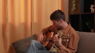 Evde gitar çalan genç bir müzisyen. Yetişkin bir gitarist odada oturup akustik gitar çalıyor enerjik şarkılar çalıyor, akorları parmaklıyor. Sürecin tadını çıkarır Yavaş çekim.
