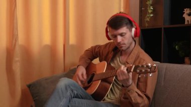 Evde gitar çalan genç bir müzisyen. Yetişkin bir gitarist odada oturmuş akustik gitar çalıyor, kulaklıkla müzik dinliyor, parmak akorları besteliyor. Yavaş çekim.