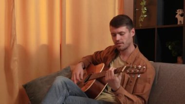 Evde gitar çalan genç bir müzisyen. Yetişkin bir gitarist odada oturup akustik gitar çalıyor, şarkı söylüyor, akorları parmaklıyor. Sürecin tadını çıkarır Yavaş çekim.