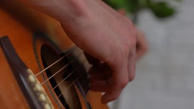 Evde gitar çalan genç bir müzisyen. Yetişkin bir gitarist odada oturup akustik gitar çalıyor, telleri parmaklıyor, melodi çalıyor, yakın çekim yapıyor. Yavaş çekim.