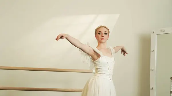 stock image This vibrant photograph captures a ballet dancer mid-pose, her arms spread wide with a dramatic flair. She is adorned in a white dress with intricate detailing and sheer sleeves that flutter as she