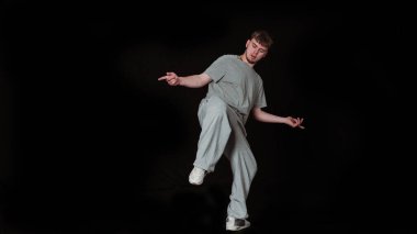 Modern bir hip hop dansında genç bir dansçının görüntüsü. Düz gri bir tişört giymişti. Basit bir siyah arkaplan dinamik duruşunu ve duygusal ifadesini vurgular..