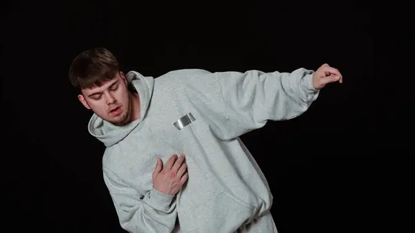 stock image Dynamic photo of a young male dancer performing a hip-hop dance move on a black background. Dressed in a comfortable gray tracksuit, he demonstrates high concentration and skill.