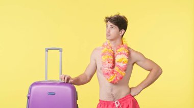 Bavulun başında bekleyen yorgun ve üzgün genç bir adam. Pembe şortlu çıplak bir adam ve sarı arka planda Hawaii lei pozu veren bir adam. Seyahat, yaz tatili.