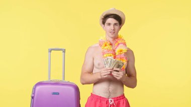 Genç adam bir tomar parayı bir hayran gibi sallıyor. Pembe şortlu üstsüz bir adam ve sarı arka planda Hawaii zambağı poz veriyor. Seyahat, yaz tatili.