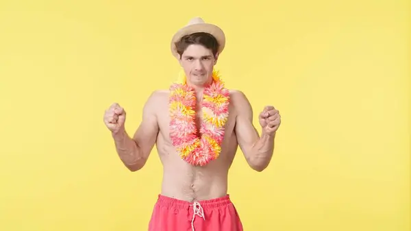 stock image A young man looks at the camera and gets very angry. Male model with bare torso in pink summer shorts and Hawaiian lei poses on yellow background. Travel, summer vacation.