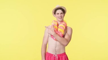 Genç bir erkek model bir çalışma alanını yanlamasına işaret ediyor. Pembe şortlu çıplak gövdeli erkek manken ve sarı arka planda Hawai lei pozu. Seyahat, yaz tatili.