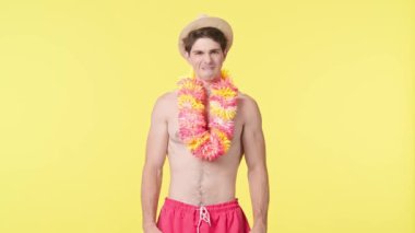Genç bir adam kameraya bakar ve çok kızar. Pembe şortlu çıplak gövdeli erkek model ve sarı arka planda Hawaii zambağı pozu. Seyahat, yaz tatili.