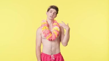 Genç bir adam sıcaktan muzdarip ve kendine el sallıyor. Pembe şortlu çıplak gövdeli erkek manken ve sarı arka planda Hawai lei pozu. Seyahat, yaz tatili, sahil tatili konsepti.