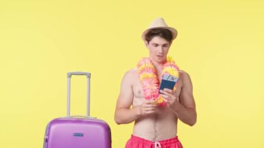Genç adam mutlu bir şekilde pasaport ve göğüs biletlerini kucaklıyor. Pembe şortlu çıplak bir adam ve sarı arka planda Hawaii lei pozu veren bir adam. Seyahat, yaz tatili.
