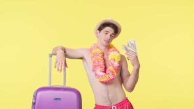 Genç adam bir tomar parayı bir hayran gibi sallıyor. Pembe şortlu üstsüz bir adam ve sarı arka planda Hawaii zambağı poz veriyor. Seyahat, yaz tatili.