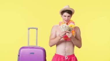 Genç adam neşeyle para saçıyor. Pembe şortlu tişörtsüz bir adam ve sarı arka planda poz veren Hawaii zambağı. Seyahat, yaz tatili.