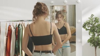 Evde aynanın önünde poz veren genç bir kadın model. Genç milenyum kadını yatak odasında aynaya bakar, kalça büyüklüğünü ölçer, mutlu bir yüz. Kişisel bakım sağlıklı güzellik konsepti.