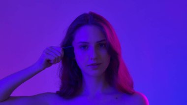 Çekici kadın model kameraya güzellik tedavisi yapıyor. Mavi neon arka planda izole edilmiş siyah taş silindirli, kamera karşısında poz veren genç bir kadın. Doğal güzellik ve cilt bakımı kavramı