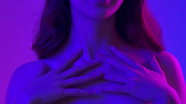 Çekici kadın model kameraya güzellik tedavisi yapıyor. Kameraya poz veren genç bir kadın pürüzsüz tenine dokunuyor ve gülümsüyor, mavi neon arka planda izole edilmiş. Doğal güzellik ve cilt bakımı kavramı