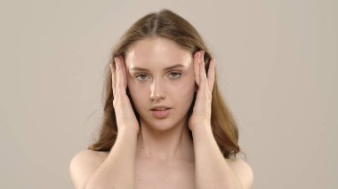 Çekici kadın model kameraya güzellik tedavisi yapıyor. Kameraya poz veren genç bir kadın beyaz arka planda izole edilmiş pürüzsüz tenine dokunuyor. Doğal güzellik cilt bakımı kavramı