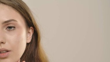 Çekici kadın model kameraya güzellik tedavisi yapıyor. Kameraya poz veren genç bir kadın geniş beyaz dişli bir gülümsemeyle, beyaz arka planda soyutlanmış. Doğal güzellik ve cilt bakımı kavramı