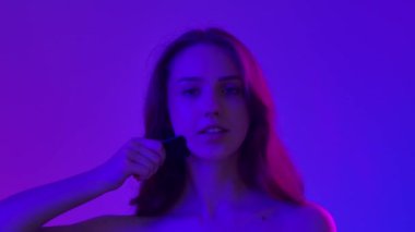 Çekici kadın model kameraya güzellik tedavisi yapıyor. Mavi neon arka planda izole edilmiş siyah taş silindirli, kamera karşısında poz veren genç bir kadın. Doğal güzellik ve cilt bakımı kavramı