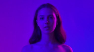 Çekici kadın model kameraya güzellik tedavisi yapıyor. Kameraya poz veren genç bir kadın boyuna lüks bir koku püskürtüyor, mavi neon arka planda izole edilmiş. Doğal güzellik ve cilt bakımı kavramı