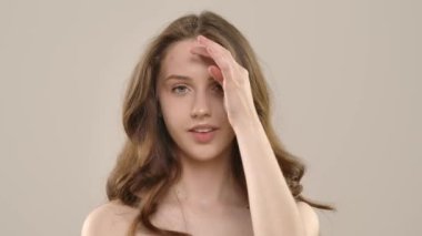 Çekici kadın model kameraya güzellik tedavisi yapıyor. Kameraya poz veren genç bir kadın beyaz arka planda izole edilmiş yüz ve omuzlarda pürüzsüz cilde dokunuyor. Doğal güzellik cilt bakımı kavramı