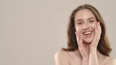 Çekici kadın model kameraya güzellik tedavisi yapıyor. Kameraya poz veren genç bir kadın beyaz arka planda izole edilmiş yüz ve omuzlarda pürüzsüz cilde dokunuyor. Doğal güzellik cilt bakımı kavramı