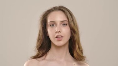 Çekici kadın model kameraya güzellik tedavisi yapıyor. Kameraya poz veren genç bir kadın boyuna lüks bir koku püskürtüyor, beyaz arka planda izole edilmiş. Doğal güzellik ve cilt bakımı kavramı