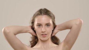 Çekici kadın model kameraya güzellik tedavisi yapıyor. Kameraya poz veren, gülümseyen, uzun ipeksi saçlarıyla oynayan, beyaz arka planda izole edilmiş genç bir kadın. Doğal güzellik ve cilt bakımı kavramı