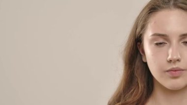 Çekici kadın model kameraya güzellik tedavisi yapıyor. Kameraya poz veren genç bir kadın pürüzsüz cilde dokunuyor, beyaz arka planda izole edilmiş. Doğal güzellik ve cilt bakımı kavramı