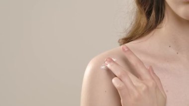 Çekici kadın model kameraya güzellik tedavisi yapıyor. Kameraya poz veren genç kadın, beyaz arka planda izole edilmiş omuz derisine vücut losyonu sürüyor. Doğal güzellik ve cilt bakımı kavramı