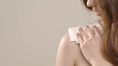 Çekici kadın model kameraya güzellik tedavisi yapıyor. Genç bir kadın kameraya poz veriyor, omuz derisini ıslak peçeteyle siliyor, beyaz arka planda izole edilmiş. Doğal güzellik ve cilt bakımı kavramı