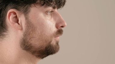 Kameraya poz veren yakışıklı sakallı erkek model. Genç yetişkin bir adam, beyaz arka planda izole edilmiş, yakın çekim. Doğal güzellik ten bakımı konsepti. Yan görünüm