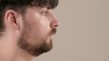 Gömleksiz, yakışıklı, sakallı erkek model sabah güzellik gösterisi yapıyor. Genç bir adam tıraş kremi sürerken beyaz arka planda izole edilmiş kameraya bakar. Yan görünüm.