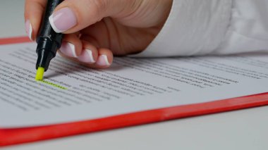 Female hand highlighting a words on paper. Close up shot of woman at the desk working with document, reading and highlighting important parts in text with yellow marker in hand. clipart