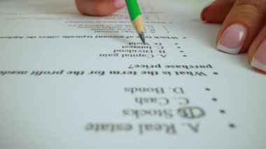 Kağıt üzerinde öğrenci el cevap sınavı. Masadaki kadının önemli bir sınav belgesiyle çalışırken, öğrencinin sınavda okuyup cevap alırken, sorular için kalem harflerle daireler çizerken yakın plan fotoğrafı..