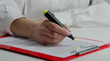 Kadın eli kâğıt üzerinde bir kelimeyi vurguluyor. Masadaki kadının elinde sarı kalemle doküman okuyup önemli kısımları işaretlediği yakın plan çekimleri..