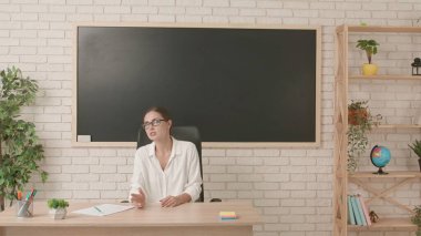 Okul öğretmeni sınıfta gençlerle konuşuyor. Bayan üniversite öğretmeni sınıfın önünde, tahtaya oturmuş öğrencilere ders veriyor. Eğitim kavramı.