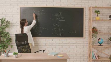 Okul öğretmeni sınıfta gençlerle konuşuyor. Kadın üniversite öğretmeni sınıfın önünde duruyor ve öğrencilere cebir dersi veriyor. Eğitim kavramı.