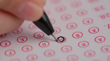 Üniversitede ya da okulda sınava giren kişi. Dişi çemberler, standart sınav kağıdında siyah kalemle doğru cevaplar veriyor. Cevap kağıdını dolduran öğrenci, doğru cevabı boyuyor, makro çekim.
