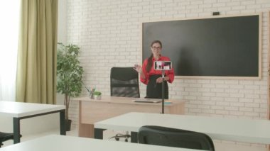 Okulda öğretmen video konferansında. Boş sınıftaki kadın öğretmen kamerayla akıllı telefon kullanarak canlı video dersi konferansını canlı yayınlıyor. Uzak bir uzak modern eğitim.