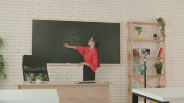 Okulda öğretmen video konferansında. Boş sınıftaki kadın öğretmen akıllı telefon kullanarak canlı video dersi konferansını canlı yayınlıyor, panoyu süngerle siliyor. Uzak bir uzak modern eğitim.