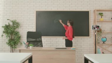 Okulda öğretmen video konferansında. Boş sınıftaki kadın öğretmen matematik örneklerini çözmek için akıllı telefon kullanarak çevrimiçi video dersi konferansı yayınlıyor. Uzak bir uzak modern eğitim.