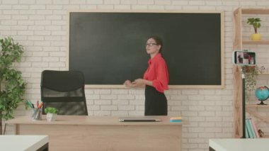 Okulda öğretmen video konferansında. Boş sınıftaki kadın öğretmen akıllı telefon kullanarak canlı video matematik konferansı yayınlıyor. Uzak bir uzak modern eğitim.
