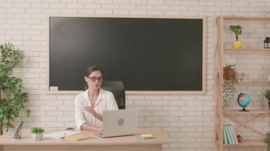 Okul öğretmeni sınıfta gençlerle konuşuyor. Sınıfta masa başında oturan, yazı tahtasının önünde dizüstü bilgisayarla konuşan bir kadın öğretmen. Eğitim kavramı.